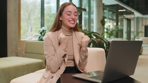 Woman Celebrates Success in Modern Office With Laptop