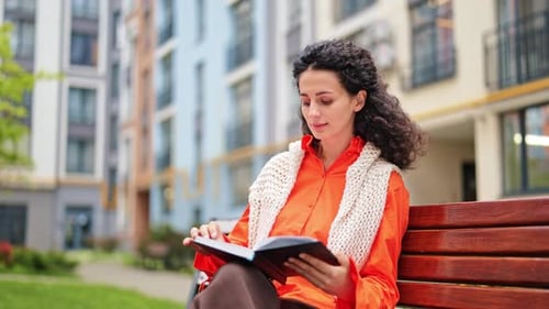 Woman Reading a Book on a Bench in a City Park