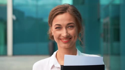Smiling Businesswoman with Folder Outside Office Building at Daytime