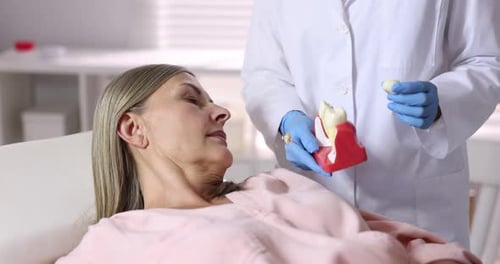 Arzt zeigt Frau in der Klinik das Modell eines Zahnimplantats, Nahaufnahme