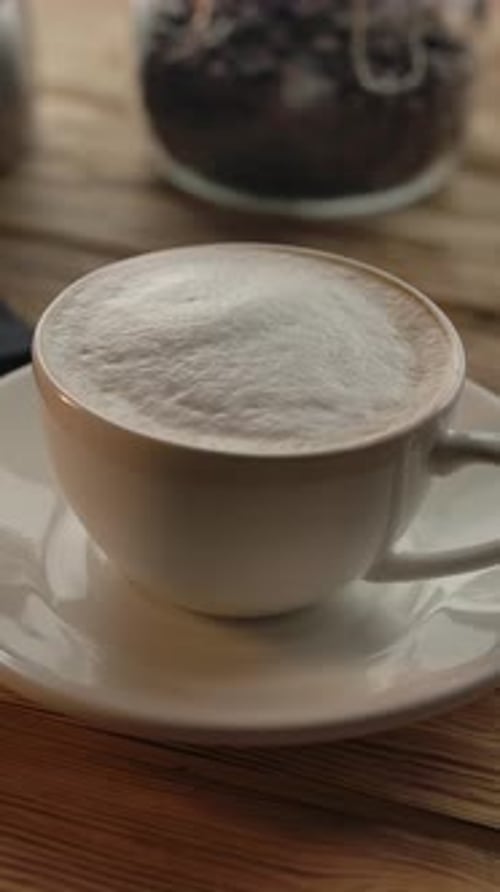 Vertikale Darstellung einer Tasse Kaffee und eines Mobiltelefons auf einem Holztisch in einem Café