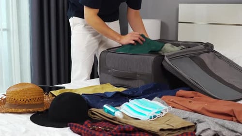 Young Adult Packing Suitcase for Travel in Bedroom
