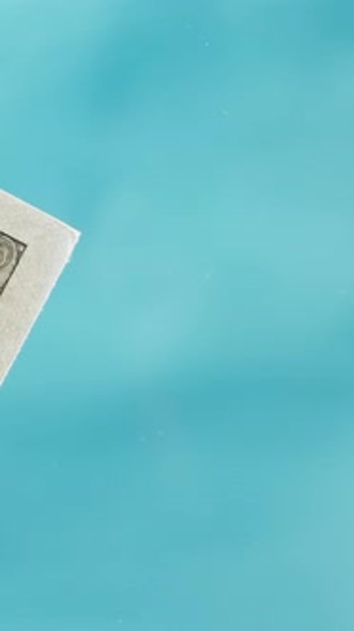 Vertical video. One hundred dollar bills are thrown onto a glass table against a blue background.