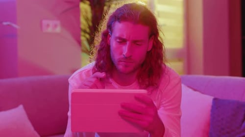 Man Using Tablet in Colorful Lit Living Room