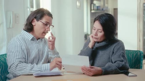 Adults Discuss Documents at Table Inside Home