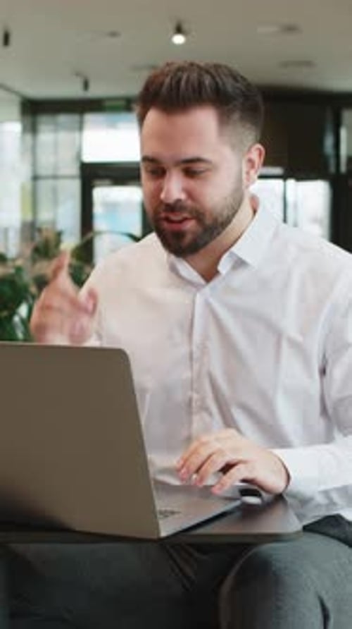 Young Businessman Using Laptop Talking on Online Communication Video Call in Modern Office Lobby