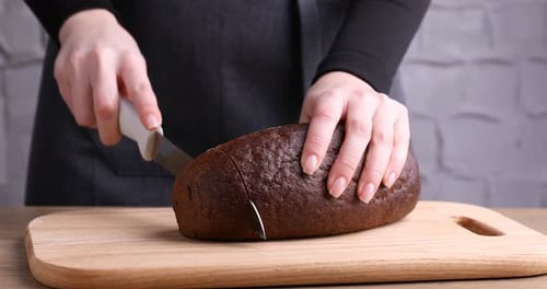 Slicing Fresh Baked Dark Bread on Wood Cutting Board
