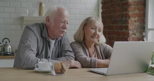 Senior Couple Video Chatting On Laptop At Home
