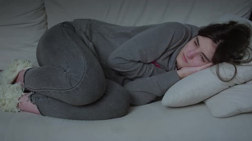 Upset Woman Lying on Couch Curled in Ball