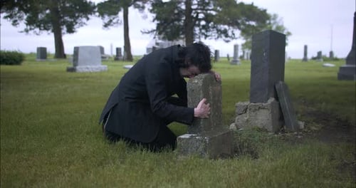 Man crying over grave, grieving death of loved one.