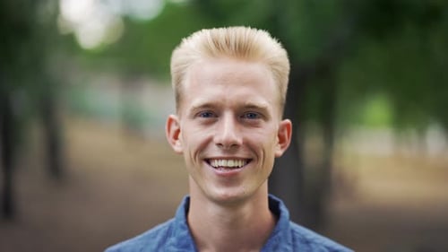Close Up Portrait Young Happy Blond Man Standing in Nature Between Park Trees Relaxes Breathes Fresh