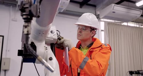 Ein Ingenieur mit Schutzhelm und Handschuhen evaluiert den Roboterschweißarm in Zeitlupe während der industriellen Arbeit