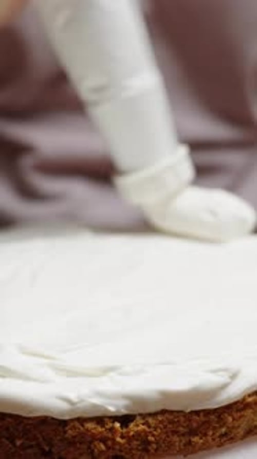 Vertical video., in a close-up shot, the woman is using a pastry bag to apply white cream along
