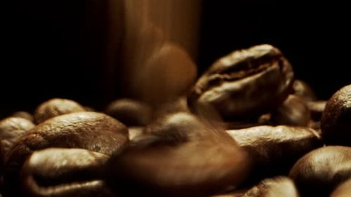 Close Camera movement through falling fresh coffee beans into a pile of beans laying on a wooden sur