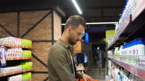 A Man Buyer Chooses Shampoo or Shower Gel in Supermarket