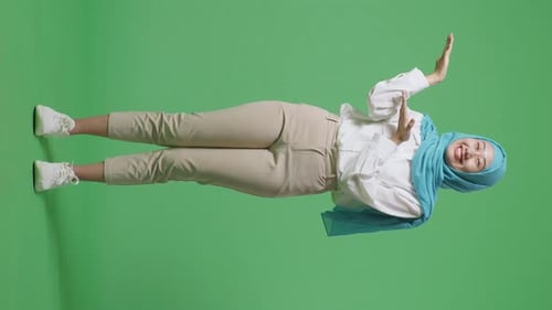 Full Body Of Asian Muslim Woman Smiling And Pointing To Side While Standing In The Green Screen