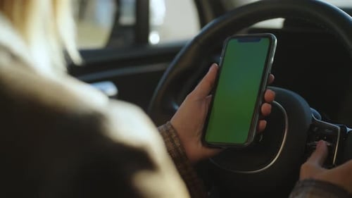 Closeup of a Woman Holding a Mobile Phone with a Green Screen in Her Hands While Sitting in a Car