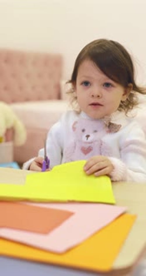 Little Child Girl Cuts Colored Paper with Scissors