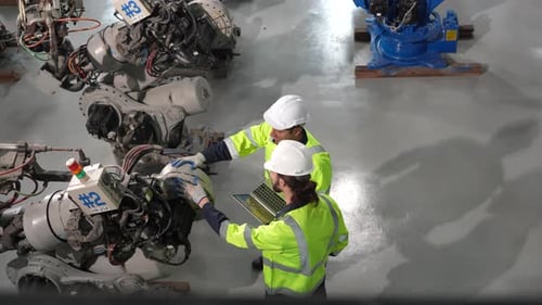 technician programs a robot arm with a digital tablet and assembly robot in a factory.