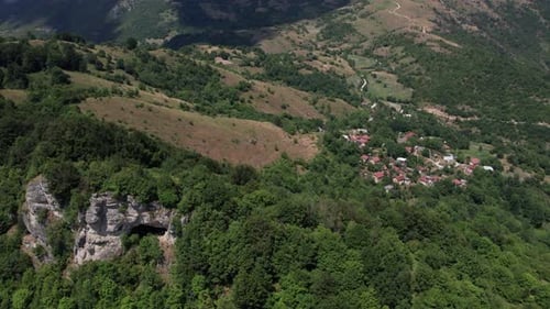 Aerial view of old mountain village near rocky cliffs and forested hills
