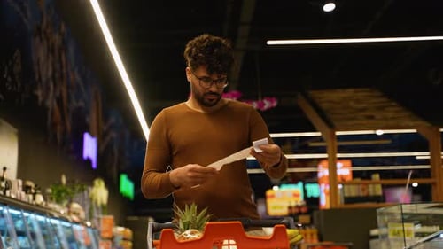 Arab Man in Brown Sweater Looking Shocked While Checking a Long Receipt in a Supermarket