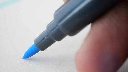 Zeitlupe eines schwarzen Markers, der eine blaue Linie auf einem Papier zeichnet
