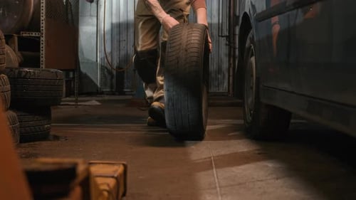Unrecognizable Mechanic Moving Automobile Tire in Workshop