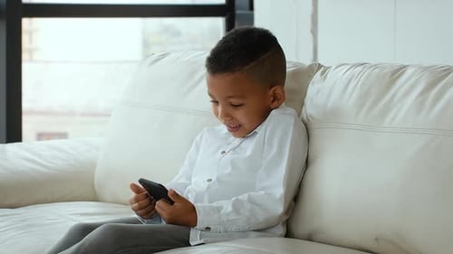 Smiling Boy Using Mobile Phone on a White Sofa