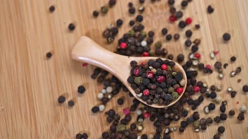A wooden spoon filled with a colorful mix of black, red, green, and white peppercorns rests on a woo
