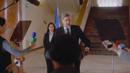 Man Speaks at Press Conference with EU Flags