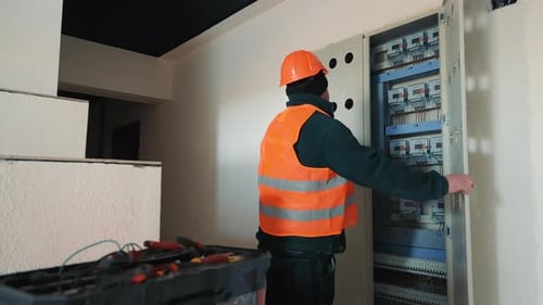 Electrician Working on a Panel An Electrician in a Safety Vest and Hard Hat is Working on an