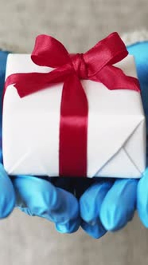 Gift Box with Red Ribbon Held in Gloved Hands