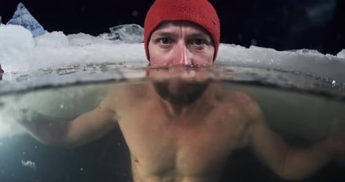 Baignade nocturne d'hiver et soin contre le froid. Un jeune homme se baigne dans le lac d'hiver la nuit et regarde le c