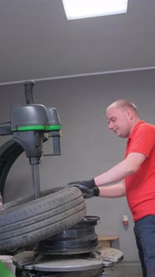 Ein Mann in einem roten Hemd repariert einen Reifen in einer Garage Vertikales Video