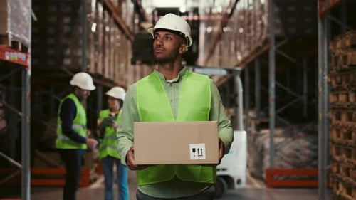 Multiethnic Worker is Walking Holding Cardboard Box in Warehouse