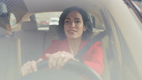 Retrato de uma bela jovem dirigindo carro pela área suburbana ensolarada. Foto de câmera feita a partir do