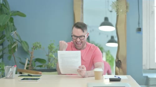 Excited Man Reads Good News at Office Desk