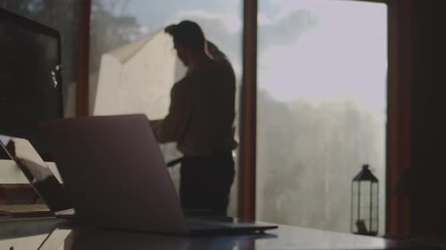 Architect Inspects Plan At Desk with Laptop