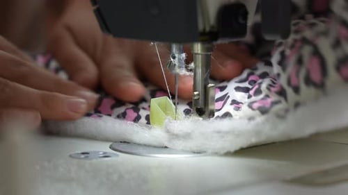 Eine weibliche Hand schiebt Material durch eine Nähmaschine