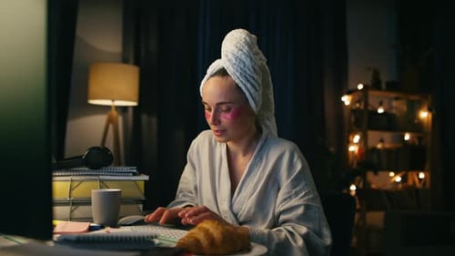 Woman in robe using computer at desk at night