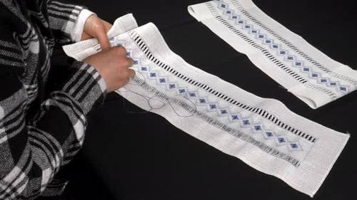 Person Sews Blue Pattern into White Fabric