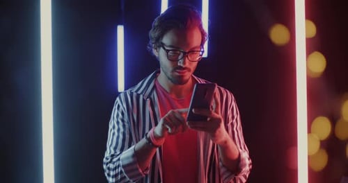 Portrait of Middle Eastern Man Using Smartphone Touching Screen and Smiling on Neon Background