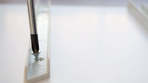 A Person is Using a Screwdriver to Screw a Screw Into a Piece of White Plastic