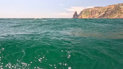 Sea Water Surface Camera Flies Over the Calm Azure Sea with Volcanic Rocky Shores on Background