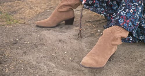Woman Wearing Cowboy Boots Sitting on Dirt