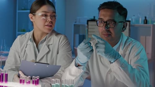 Researcher Analysing Sample Holding Test Tube, Female Coworker Taking Notes