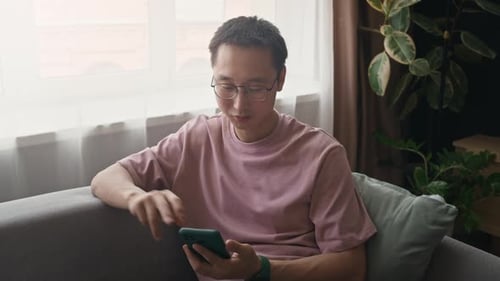 Man on Sofa Uses Phone at Home Daytime