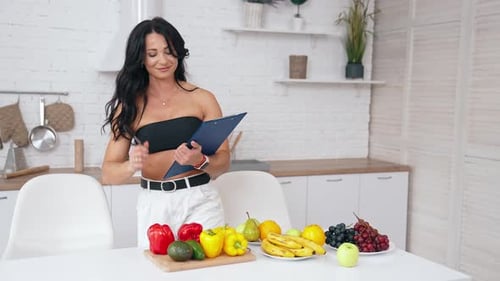 Healthy food at home. Happy brunette woman is making notes in modern kitchen.