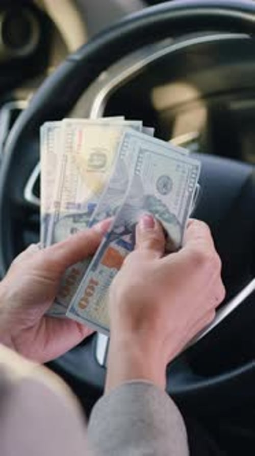 Closeup Female Hands Behind Steering Wheel in Luxury Car Counting Cash Financial Profits in the
