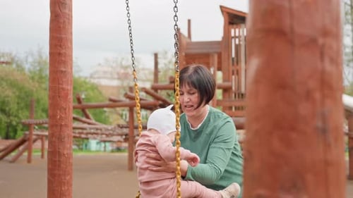 Woman and Baby on Tire Swing in Playground